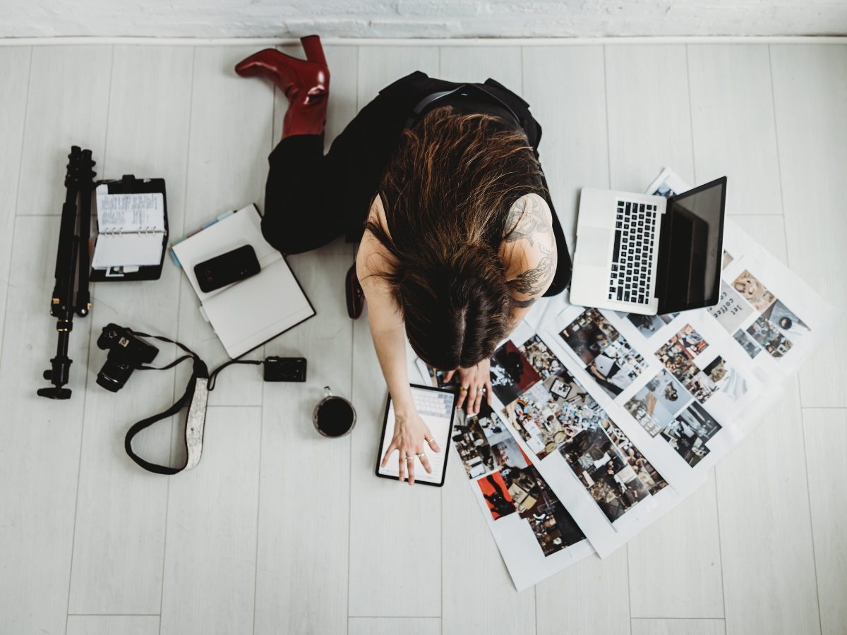 Social media manager planning monthly content workflow with phone laptop and printed photos